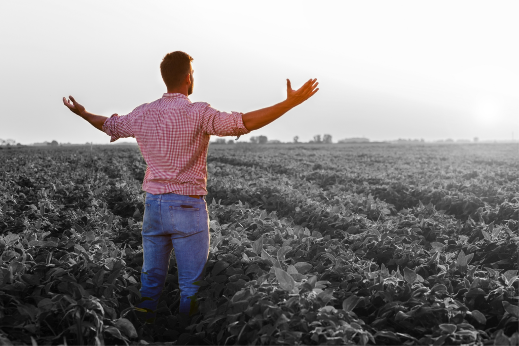 Colourized farmer standing in black and white soybean field with arms out.